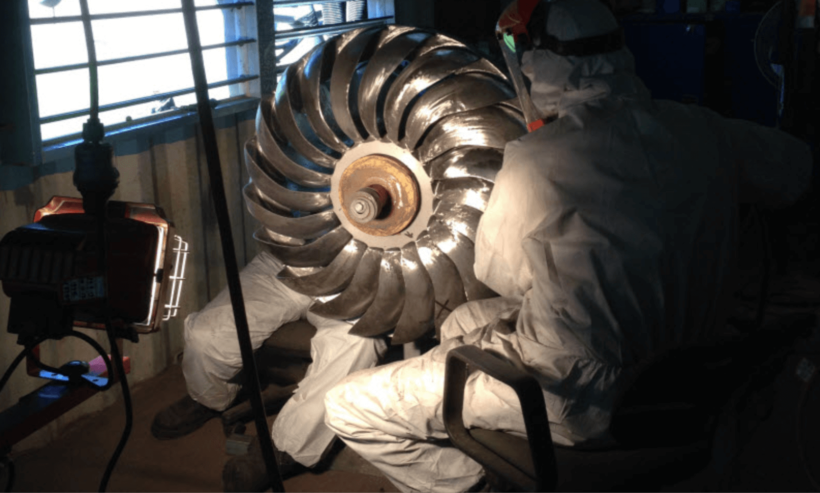 Two workers fitting a pelton turbine into a container